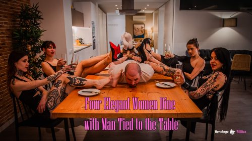 Man tied up and gagged on a table while four elegant women humiliate him with feet and bondage during a luxurious dinner.